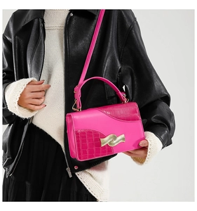 Detail of rose pink handbag with crocodile texture and golden wavy metal lock
