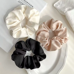 Tre eleganti elastici in raso di seta nei colori crema, oro e nero su un vassoio bianco