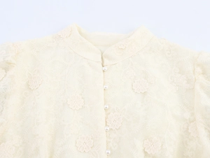 Gros plan sur la broderie en dentelle florale et les boutons de perles d'une robe beige