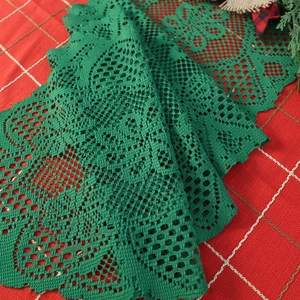 Green knit Christmas table runner with lace tassels on red plaid tablecloth background