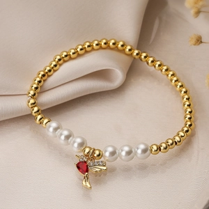 Elegant gold bird charm bracelet with white pearls and red heart stone on silk background