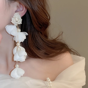 Close-up of elegant long flower pearl tassel earrings worn by a model in soft lighting