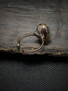 Macro shot of an adjustable vintage ring featuring a raw green gemstone on weathered wood