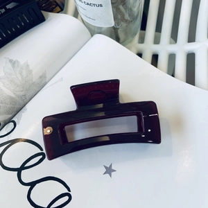 Close-up of deep wine red glossy hair claw clip with hollow rectangular design on a book