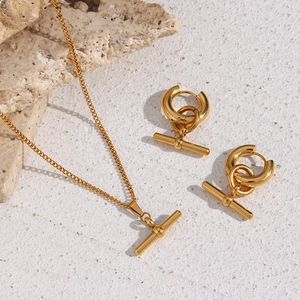 Polished gold T-bar necklace and matching earrings set on a minimalist natural stone