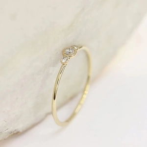 Elegant gold-finished ring with three micro-set zircon stones on white textured stone