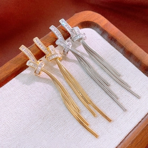 Elegant gold and silver plated knot earrings with zircon tassels on a white linen tray