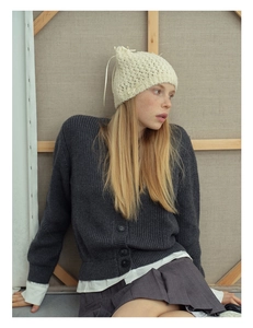 Detail of a beige knit cat ear beanie with ribbon bow ties and a dark gray cardigan