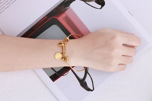 Detailed view of a gold bangle featuring a 3D heart and coin pendant on a model's wrist