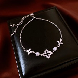 Detail of silver clover flower bracelet with pearls on red silk, macro jewelry view