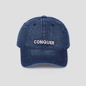 Detailed view of white CONQUER embroidery on washed navy denim baseball cap