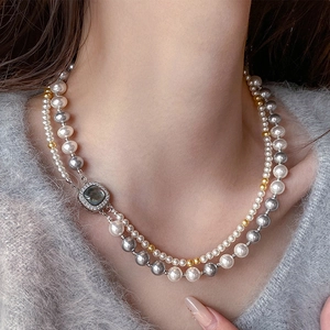 Dettaglio della collana di perle a doppio strato con pendente quadrato su maglione grigio