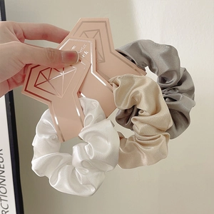 Three-pack of satin silk scrunchies in white, champagne, and grey on elegant display cards