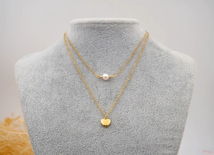 Detail of layered gold titanium steel necklace with freshwater pearl and heart charm