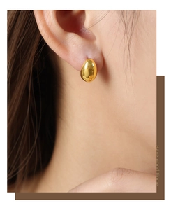 Close-up of polished gold teardrop stud earrings worn by a model in a minimalist style
