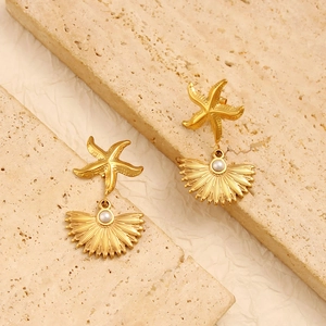Golden sea star and shell drop earrings with white pearl accents on stone background