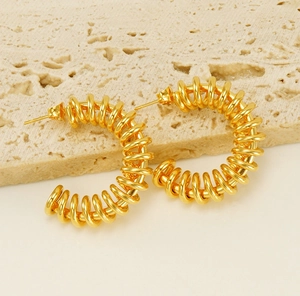 Detail of 18K gold-plated stainless steel spring hoop earrings on a stone background