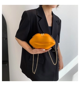 Detail der orangen lippenförmigen Handtasche mit Goldkette auf schwarzem Blazer