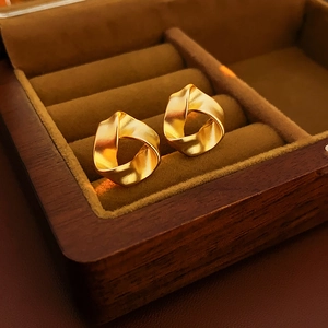 Detail of twisted gold ribbon stud earrings on luxury dark wood jewelry display case