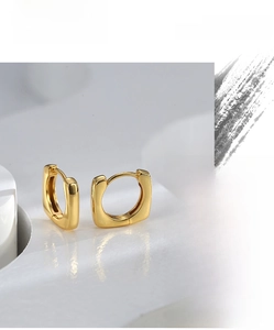 Detailed macro view of polished gold square hoop earrings on marble texture