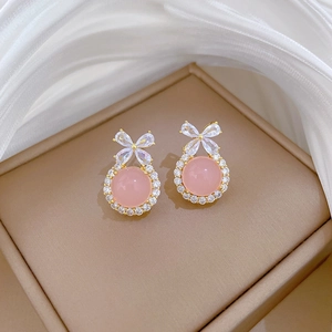 Detail of gold bow earrings with pink gemstone and zircons in a beige jewelry box
