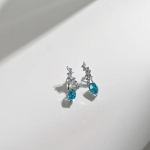 Macro detail of silver stud earrings featuring light blue pear-shaped zircon stones