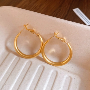Close-up of matte gold hoop earrings resting on a white ceramic textured tray