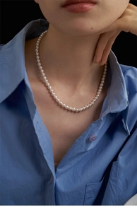 Close-up of vintage pearl necklace on model neck with elegant blue shirt detail