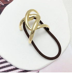 Detail of a brown elastic hair tie with a gold abstract curved metal accessory