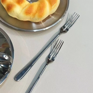 Close-up of polished stainless steel fruit forks with glossy finish on a textured surface
