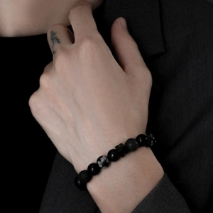 Close-up of men's matte black obsidian and volcanic stone bracelet with snowflake bead