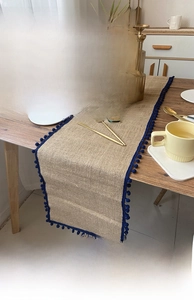 Close-up of natural jute table runner with blue pom-poms and elegant table setting