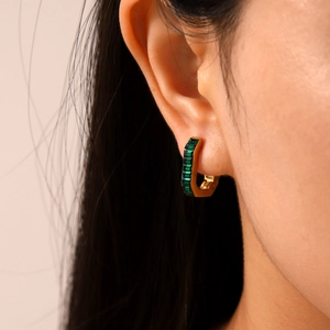 Close-up of gold U-shaped earrings with channel-set green rectangular zircon stones