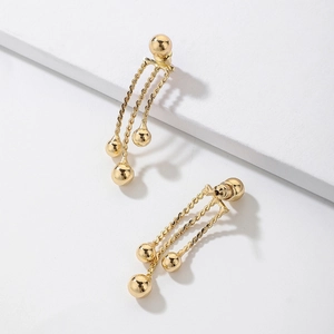 Detail of gold fringe earrings with metallic beads on a minimalist white background