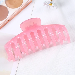Large pink plastic hair claw clip with glossy finish and curved teeth on white fabric