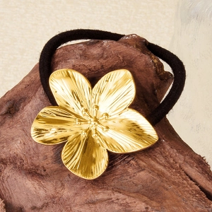 Close-up of golden metal flower charm with black elastic hair tie on wood surface