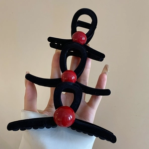 Three sizes of black flocked hair claws with red beads held in hand for size comparison