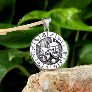 Silver zodiac pendant with comedy tragedy masks on a branch over a natural rock