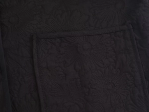 Close-up of black jacket fabric featuring 3D embossed daisy floral embroidery and quilting