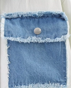 Detailed view of a blue denim pocket with silver button and frayed edges on white fabric