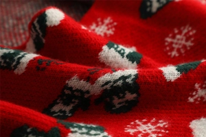 Close-up of soft red knit fabric with white snowflake and green Christmas tree patterns