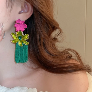 Gros plan sur les boucles d'oreilles bohème avec fleurs roses et franges vertes sur modèle