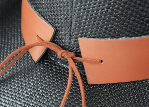 Close-up of black woven straw cowboy hat featuring brown leather belt and knot detail