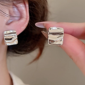 Macro shot of silver square stud earrings with liquid ripple texture and metallic luster