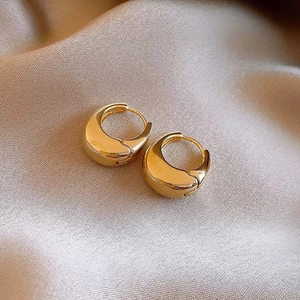 Minimalist geometric C-shape gold hoop earrings on a silky beige fabric background