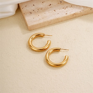 Close-up of golden chunky hoop earrings on a textured stone with silk fabric