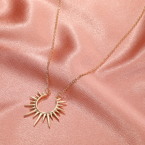 Élégant collier avec pendentif soleil en or rose sur fond de tissu en soie rose doux