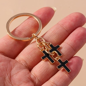 Close-up of gothic cross keychain with black enamel drips and polished gold plating