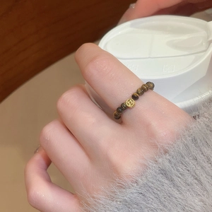 Detailed close-up of tiger eye beaded ring with a gold coin charm on the finger