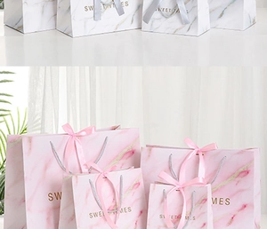 Close-up of marble gift bags with golden Sweet Times logo and satin ribbon bows